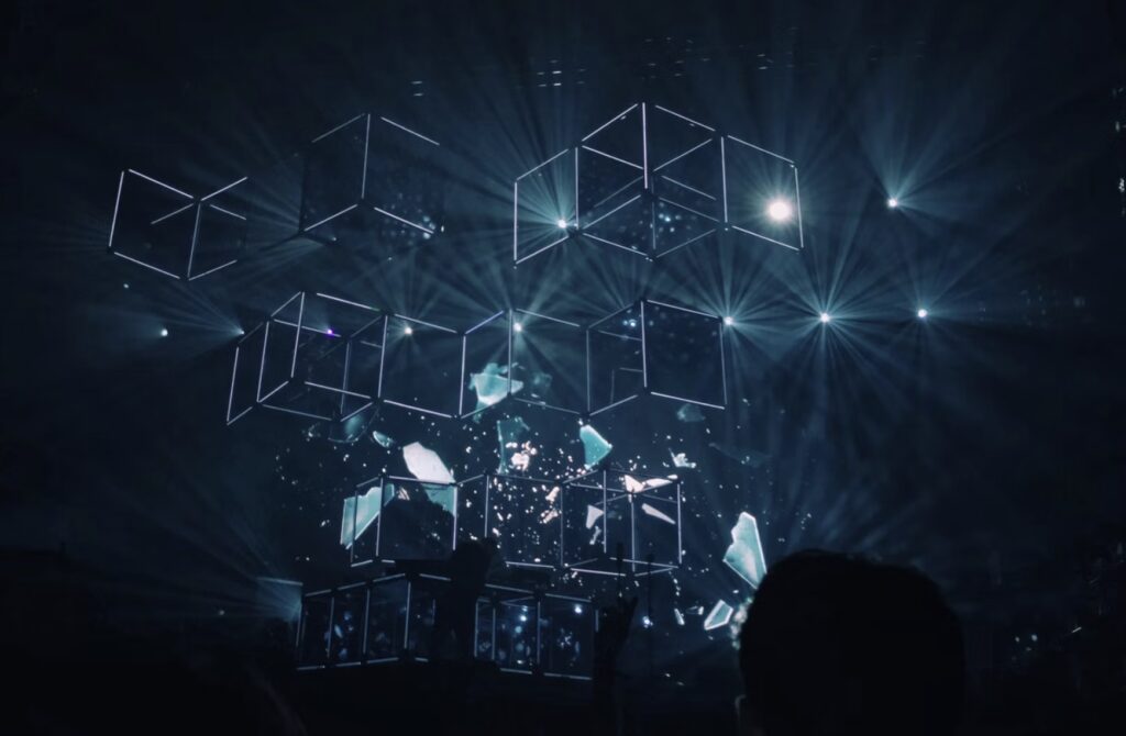 Digital-looking cubes against a black background with spotlights, and shattered glass falling from the lower cubes