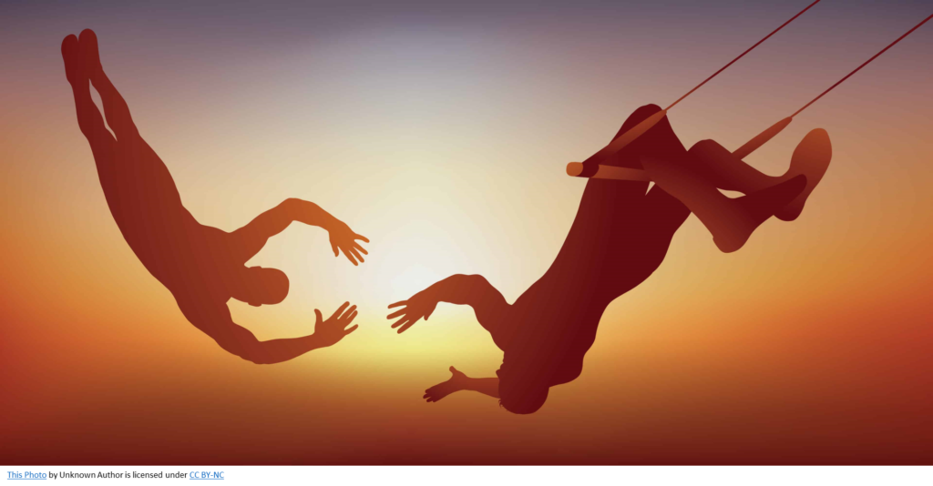 Silhouette of two people in mid-air, one on a trapeze, catching another with their hands reached out